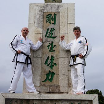 A picture of two karate master posing in front of GenChoi monument